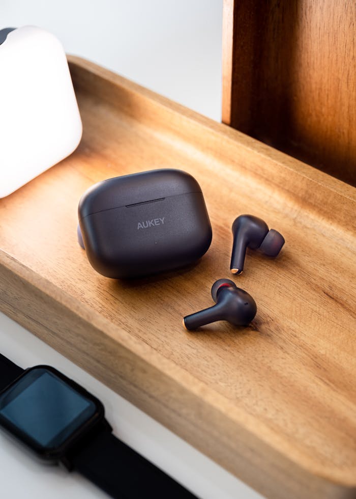 Close-up of Aukey wireless earbuds on a stylish wooden tray with a smartwatch nearby.